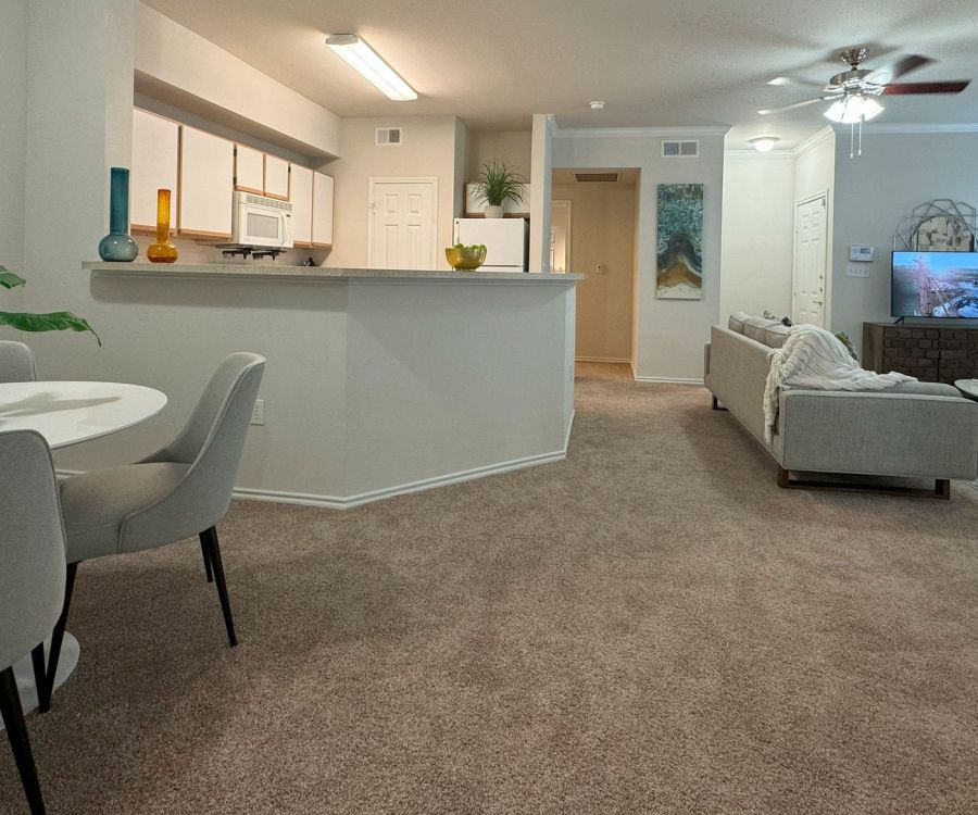 Modern living room and dining area with carpet, neutral tones, and wall decor. TV and sofa in the background.