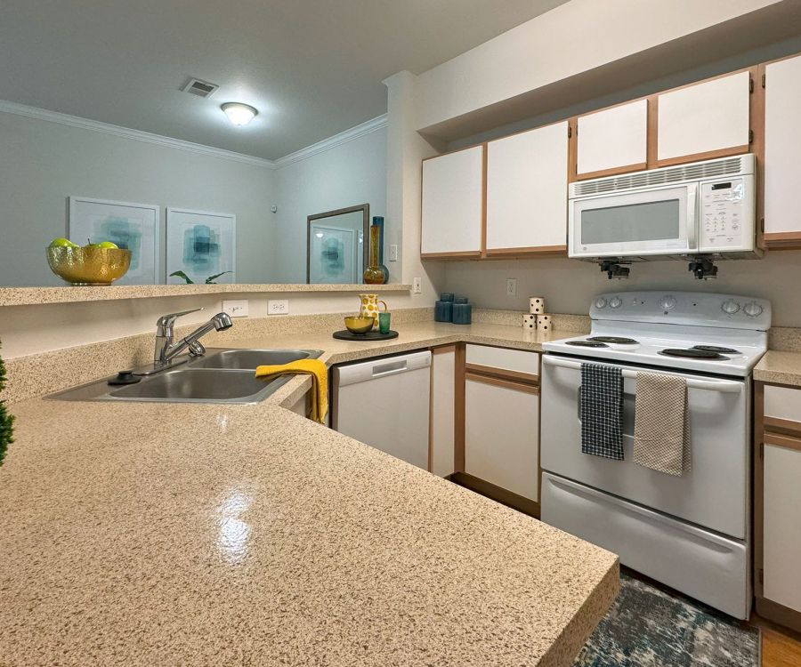 A modern kitchen with beige countertops, white cabinets, an electric stove, and a microwave. Decor accents are visible.